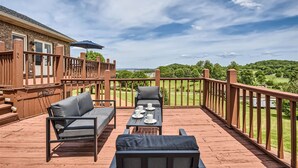 Una terraza de madera con mobiliario exterior, una mesa con tazas y platos, y vistas a un paisaje verde.