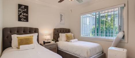 A hotel room with two beds, a ceiling fan, a window with blinds, and a wall-mounted air conditioner.