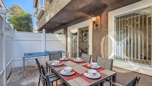 Eine Terrasse im Freien mit einem Esstisch für sechs Personen, umgeben von Stühlen, und einem kleinen Tisch mit einem Gesellschaftsspiel.