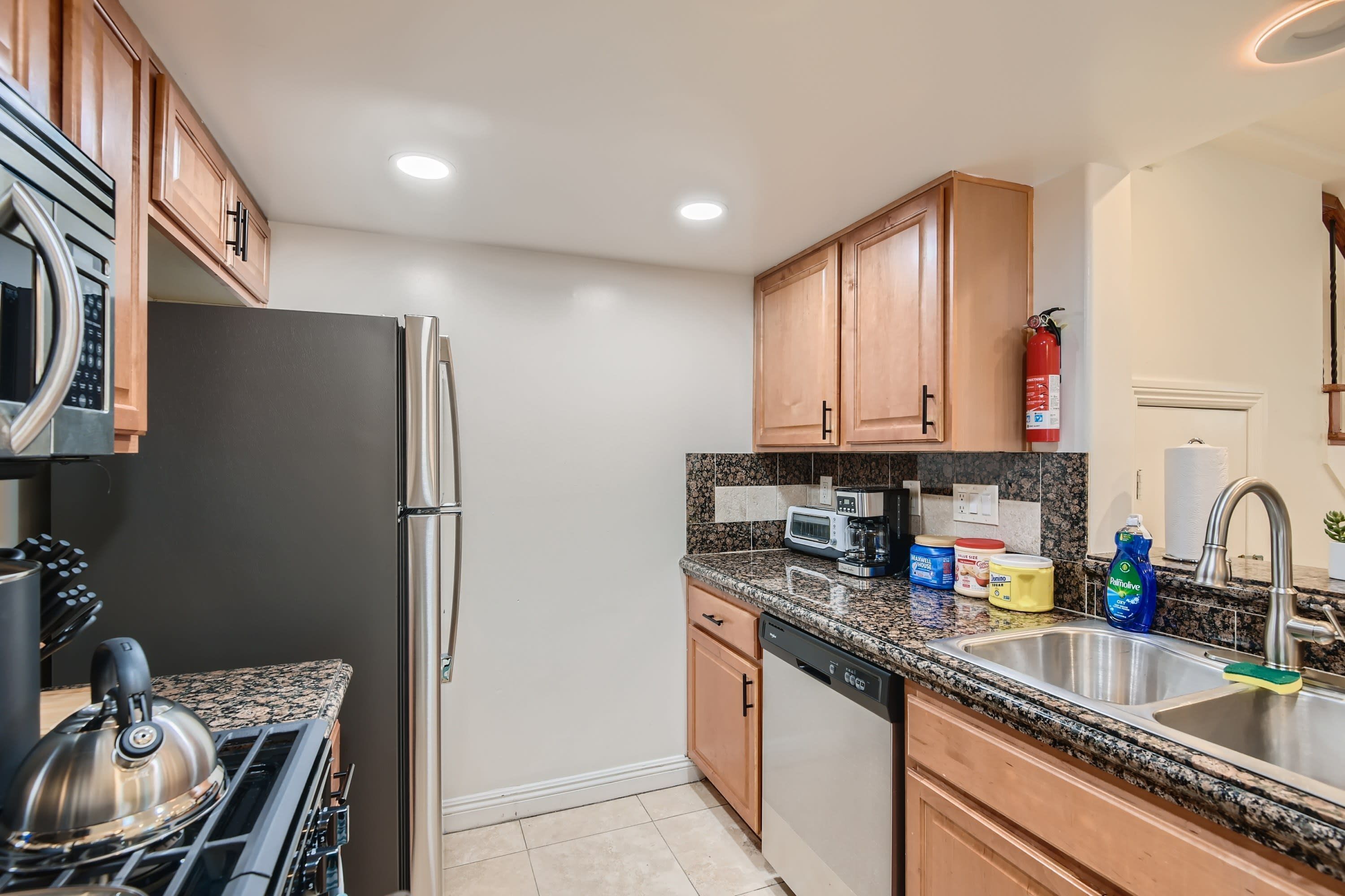 A modern kitchen with granite countertops, stainless steel appliances, wooden cabinets, and a built-in dishwasher.