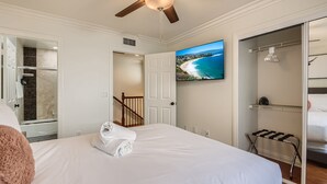 Ein Hotelzimmer mit einem großen Bett, einem Deckenventilator, einem an der Wand befestigten Fernseher und Blick auf einen Strand.