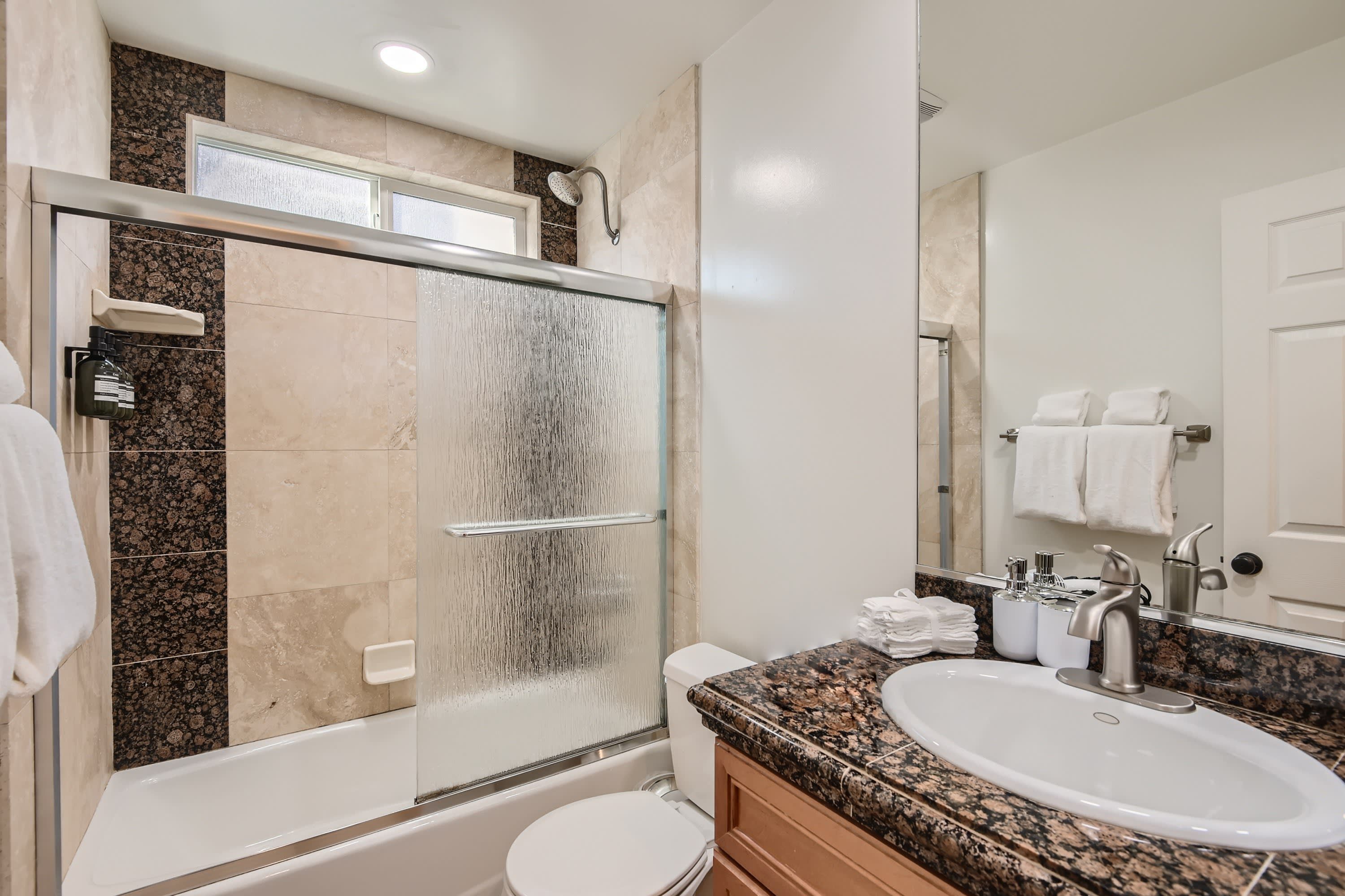 Un baño moderno con ducha de vidrio, lavamanos blanco y encimera de mármol.