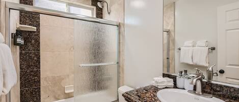 Un baño moderno con ducha de vidrio, lavamanos blanco y encimera de mármol.