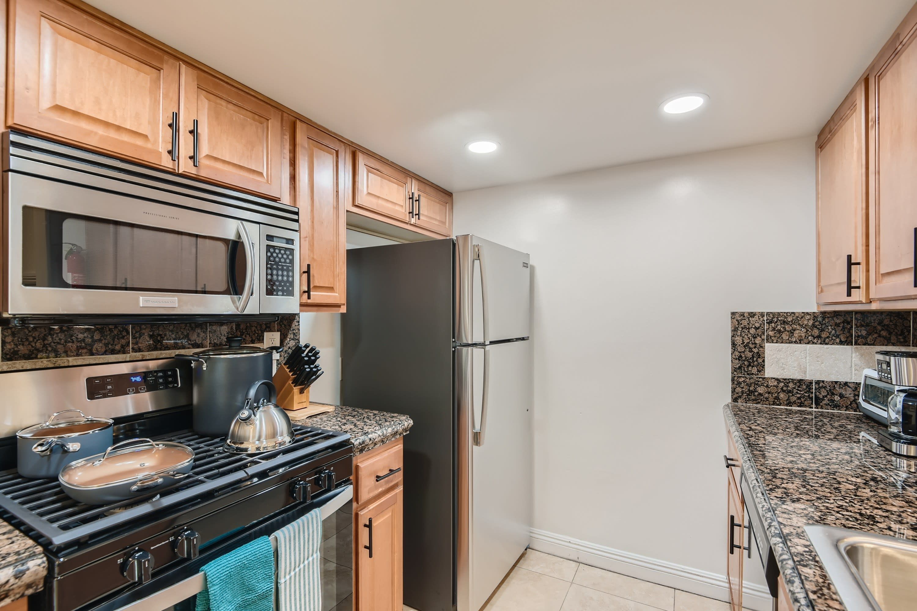 A modern kitchen with wooden cabinets, stainless steel appliances, granite countertops, and a tiled backsplash.