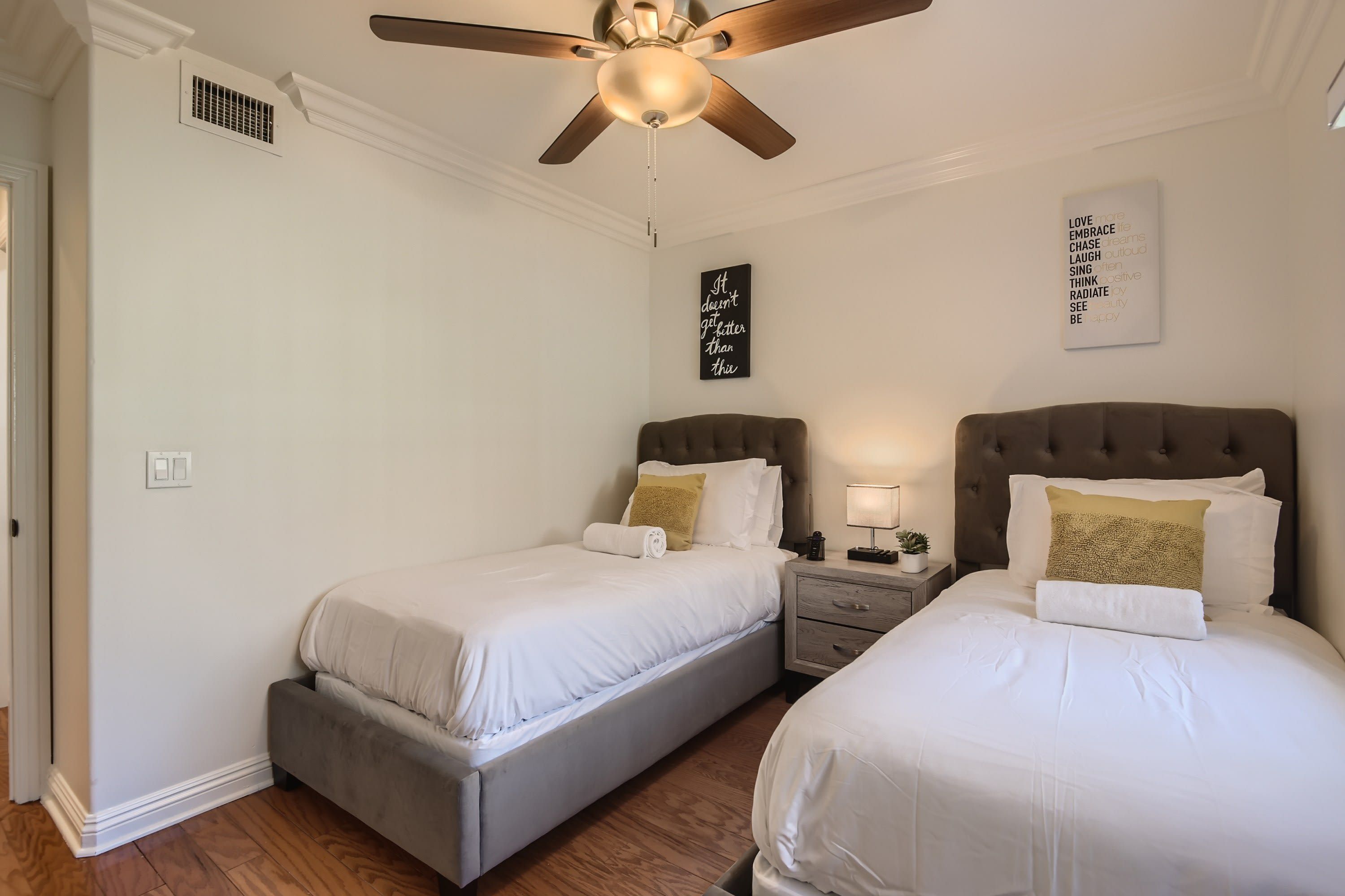 Een slaapkamer met twee bedden, een plafondventilator en inspirerende muurdecoratie.