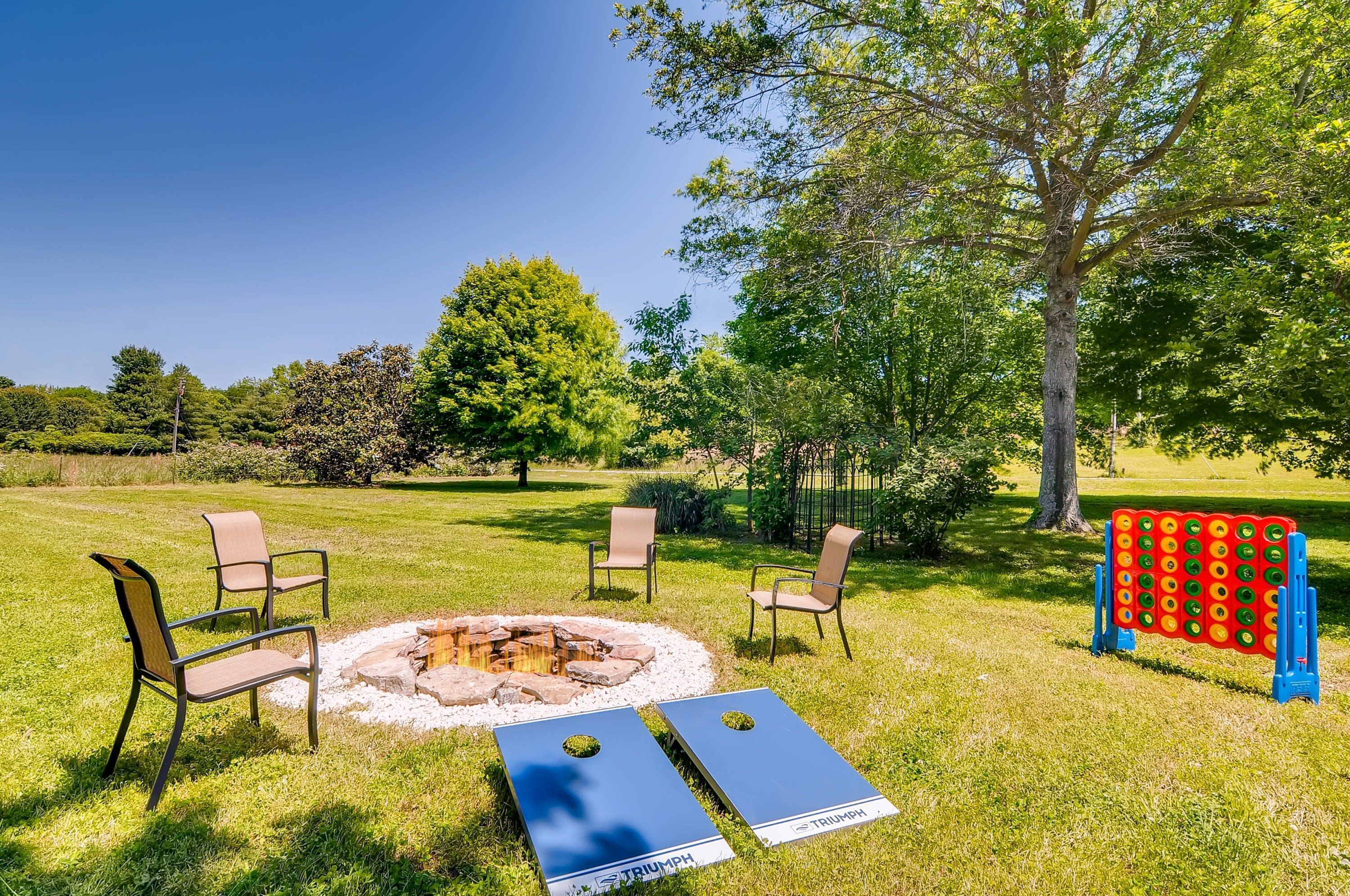 A fire pit surrounded by chairs and a board game in a grassy outdoor area.