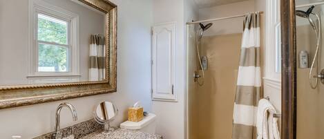 A bathroom with a granite countertop sink, a large mirror, a toilet, and a glass-enclosed shower with a striped curtain.