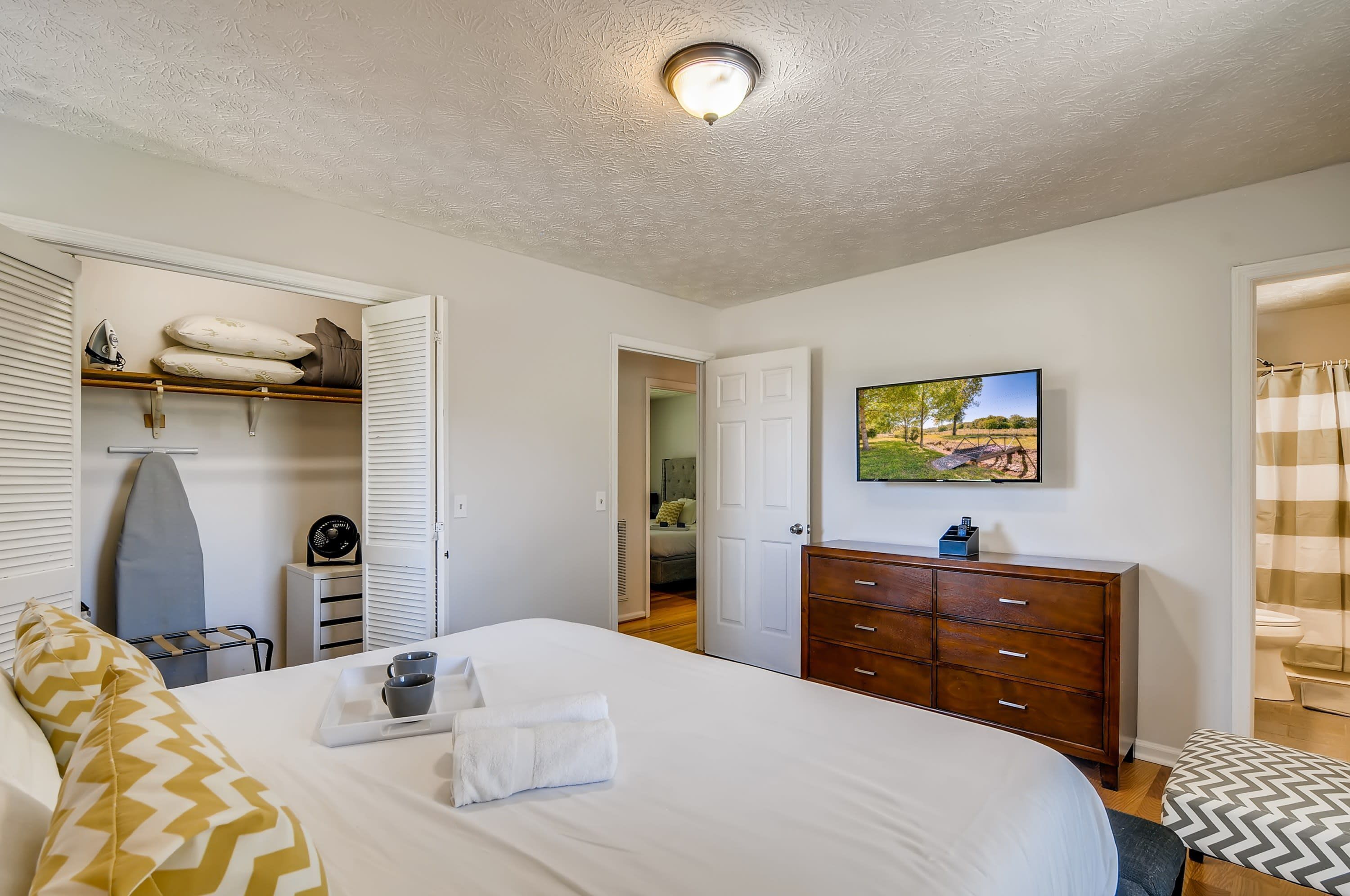 A bedroom with a bed, a dresser, a television, and a door leading to another room.