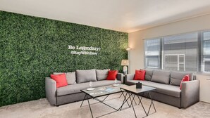 Een moderne woonkamer met een groene wand, grijze banken, rode kussens en een salontafel.