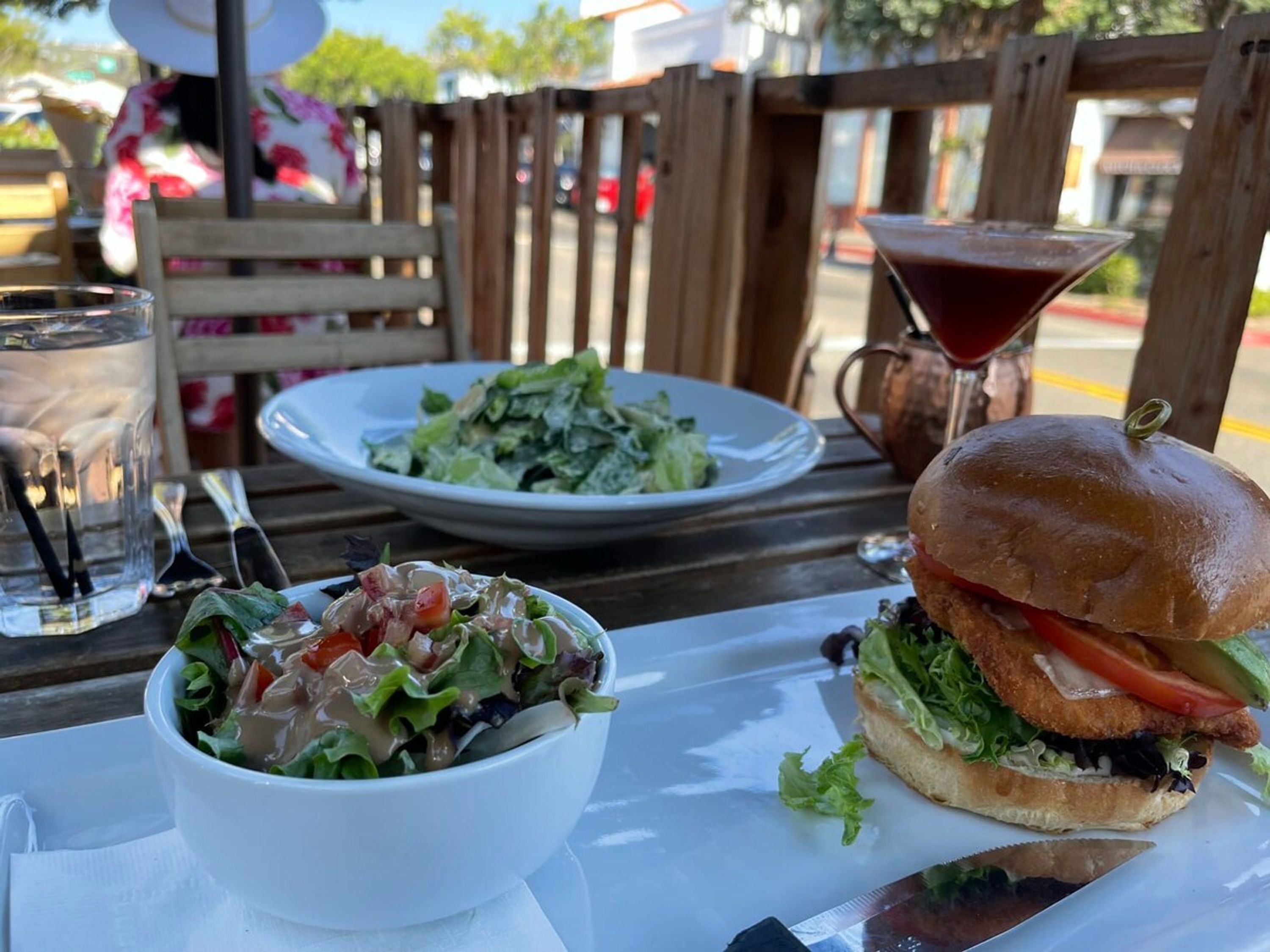 A table with a salad, a burger, a martini glass, and a water glass.