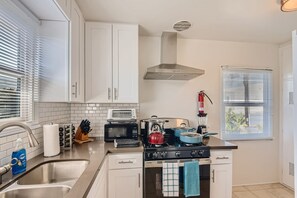 A modern kitchen with white cabinets, a stainless steel sink, a stove, and a microwave. - Walk to Beach - King Apt In 1 Area - AC (San Clemente)