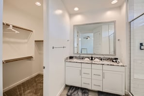 Uma casa de banho moderna com armários brancos, bancada de granito e um espelho grande.