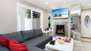 A modern living room with a grey sofa, a fireplace, and a television displaying a beach scene. - Costa Mesa -newport- Patio - Free Parking-cm-2 (Costa Mesa)