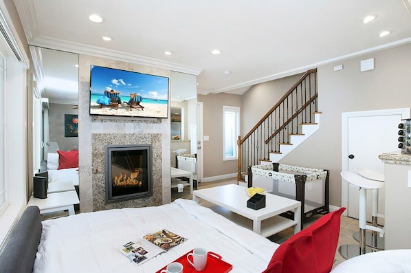 Una habitación de hotel con chimenea, televisor montado en la pared, escalera y zona de comedor.