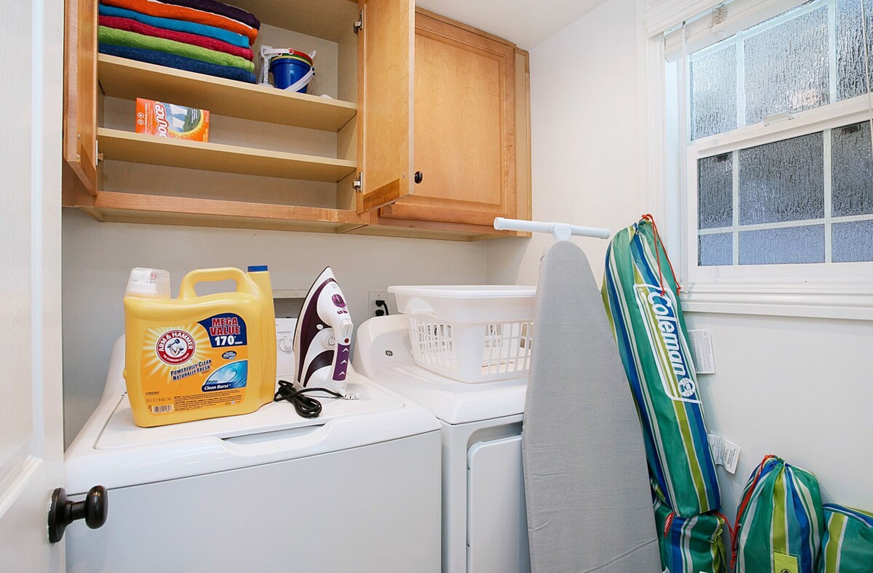 A laundry area with a washing machine, a dryer, a basket, and a shelf with folded clothes and a box of detergent.