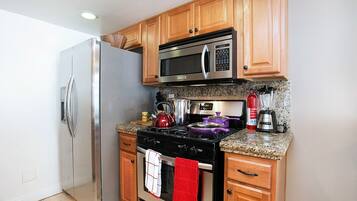 A kitchen with wooden cabinets, stainless steel appliances, granite countertops, and a red towel hanging on the oven handle.