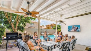 Une terrasse couverte, aménagée avec du mobilier d’extérieur, un barbecue et une piscine en arrière-plan.