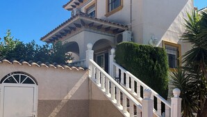 Una casa de dos pisos con fachada blanca, techo de tejas y una escalera blanca que conduce a la entrada.