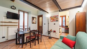 Ein gemütliches Wohnzimmer mit Essbereich, einer Küche im Hintergrund und einem an der Wand befestigten Fernseher.