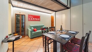Ein Essbereich mit Tisch für vier Personen, einem grünen Sofa und einem Schild mit der Aufschrift 'Bitter Campari'.