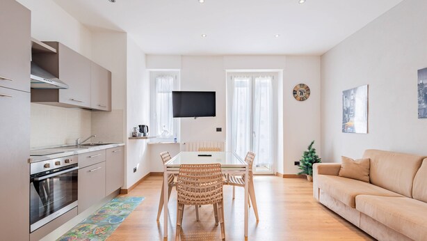 Una cocina moderna con horno empotrado y comedor con mesa de vidrio y sillas de mimbre.