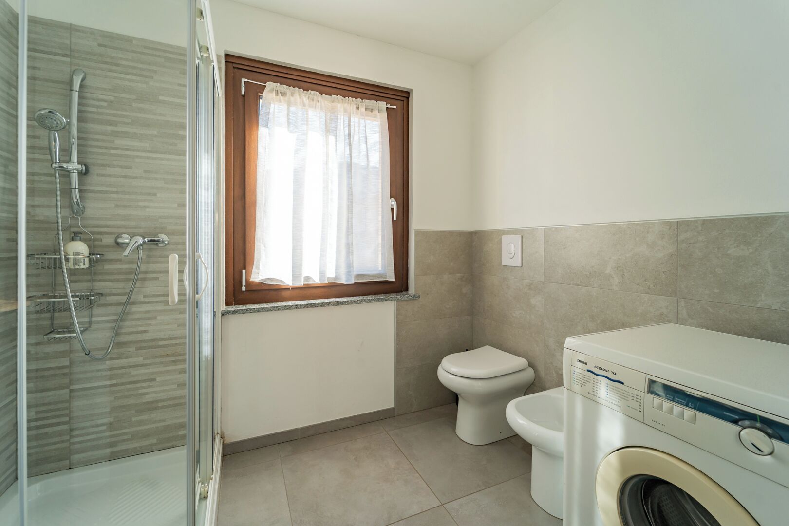 A bathroom with a glass shower enclosure, a toilet, and a washing machine.