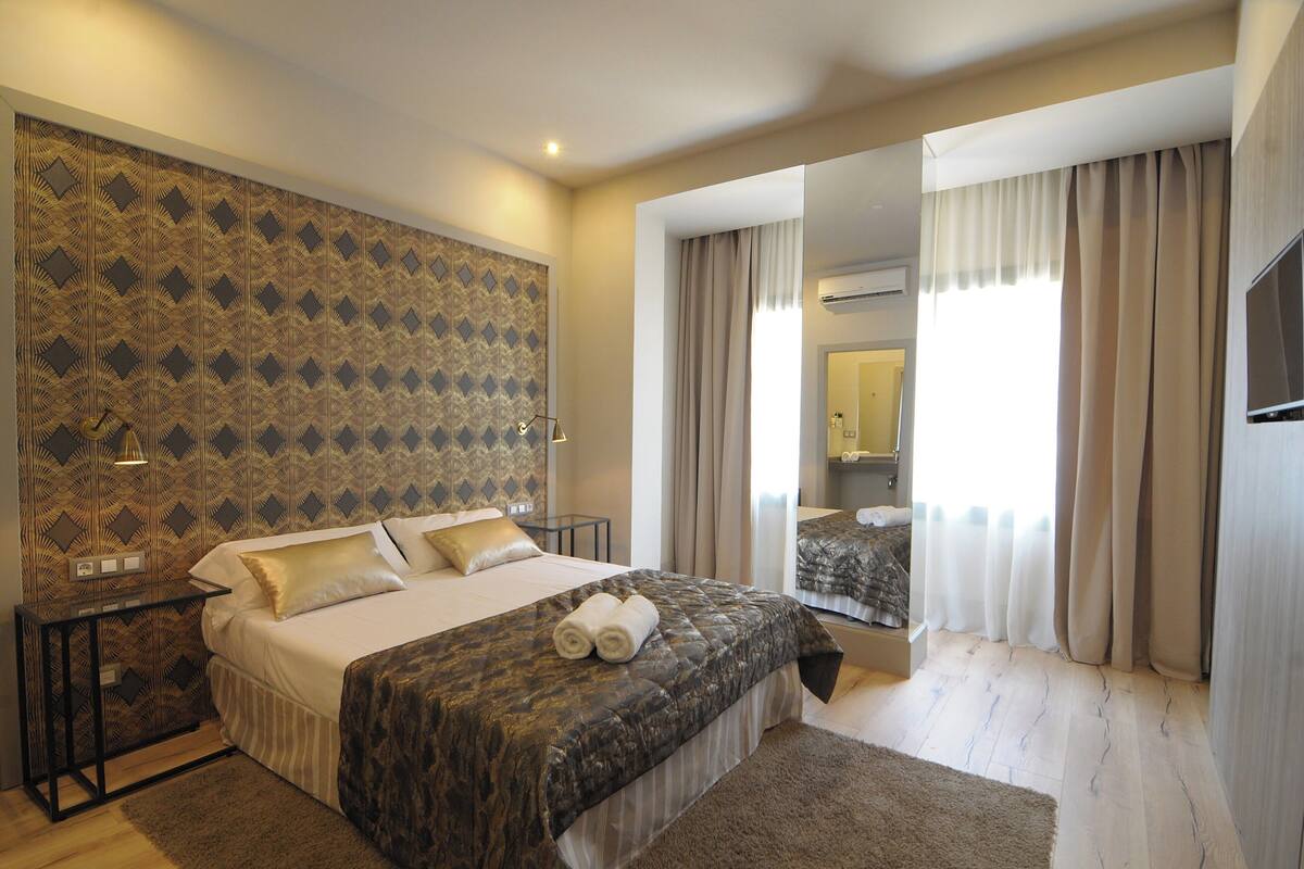 A hotel room with a large bed, a nightstand, a mirror, and a view of the bathroom.