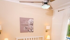 A bedroom with a bed, nightstands, a ceiling fan, and a window with curtains.