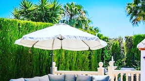 A curved sofa with cushions, a matching coffee table, and a large umbrella in an outdoor patio area with a pool.