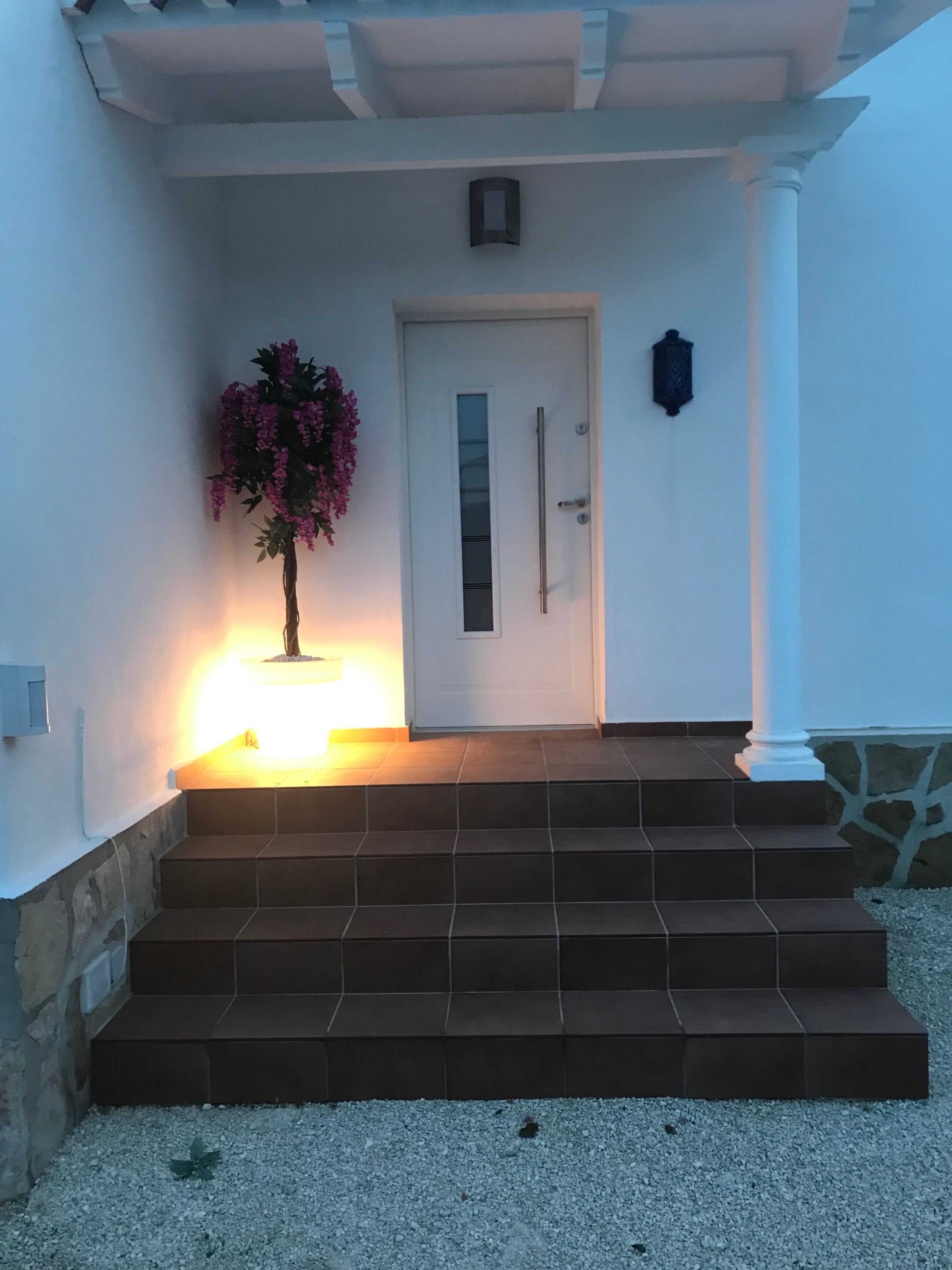 A building entrance with a white door, steps leading up to it, and a wall-mounted light fixture.