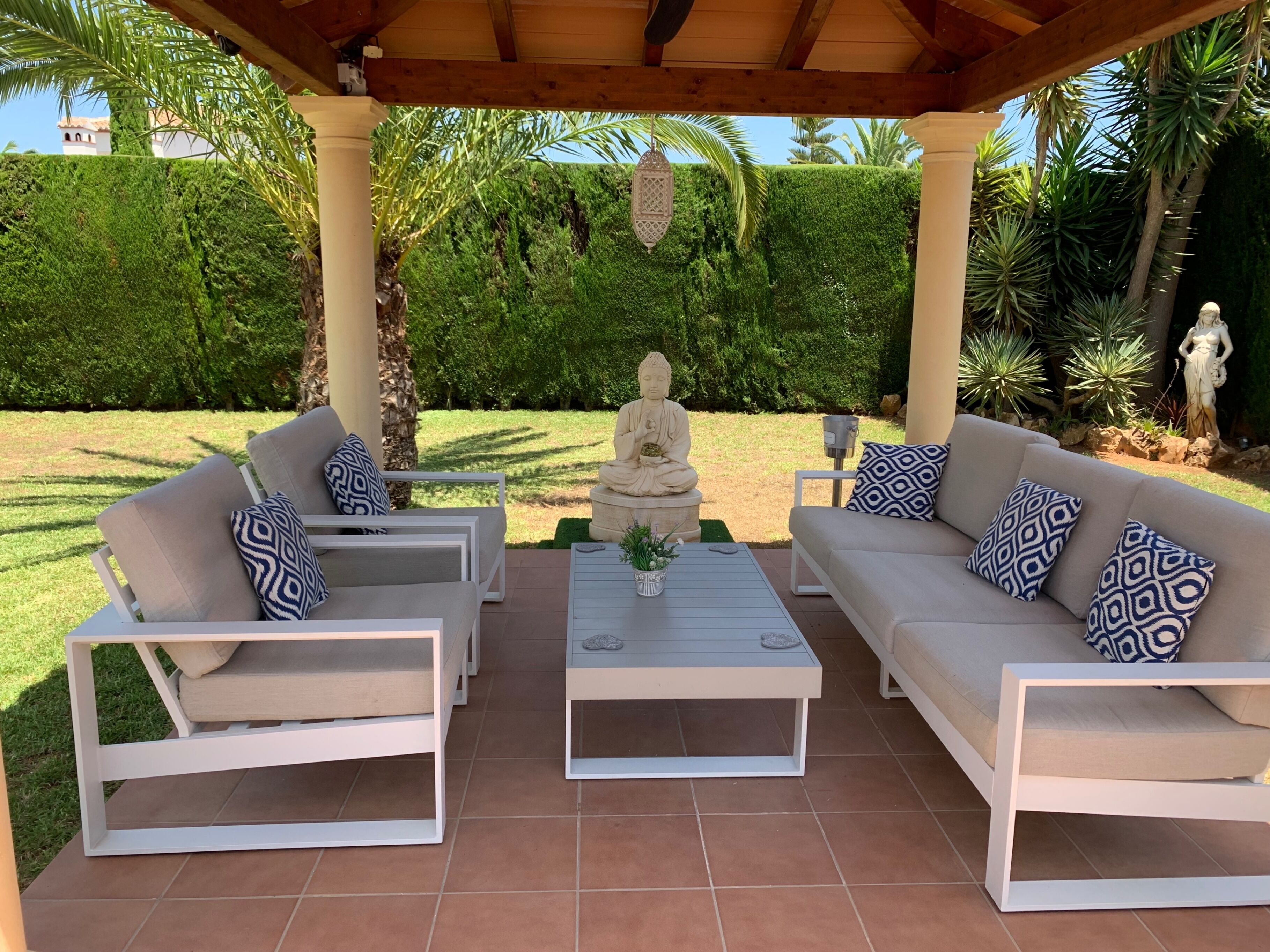 Een terras met witte meubels, een Boeddhabeeld en een verzorgde tuin.