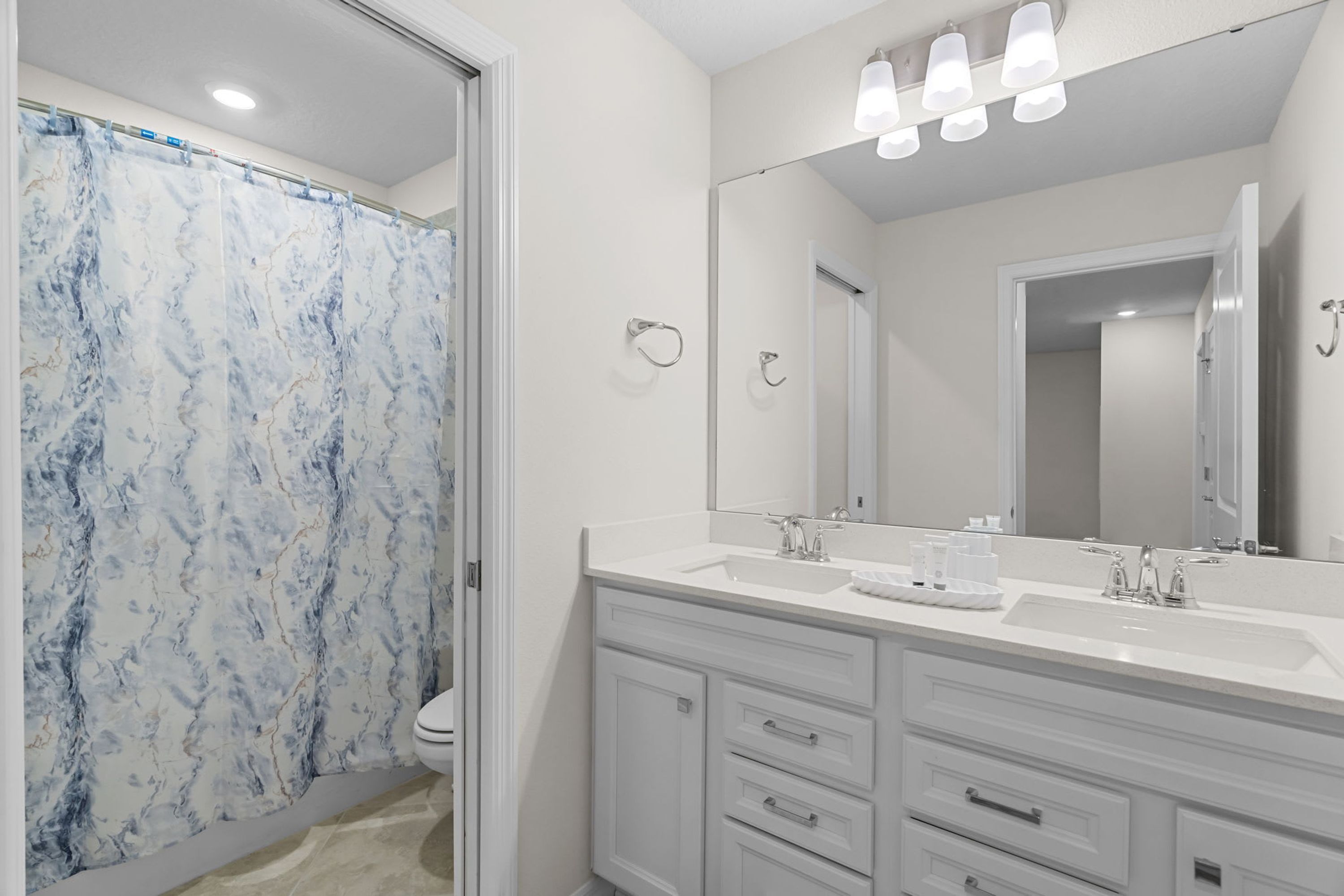 A bathroom with a white vanity, a large mirror, and a shower curtain with a marble pattern.