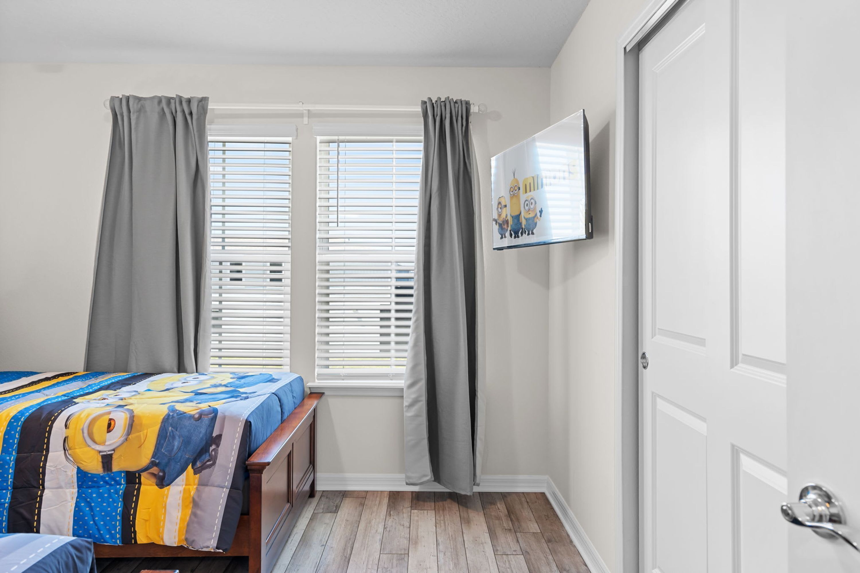 Un dormitorio con una cama, un banco, un televisor en la pared y una puerta.