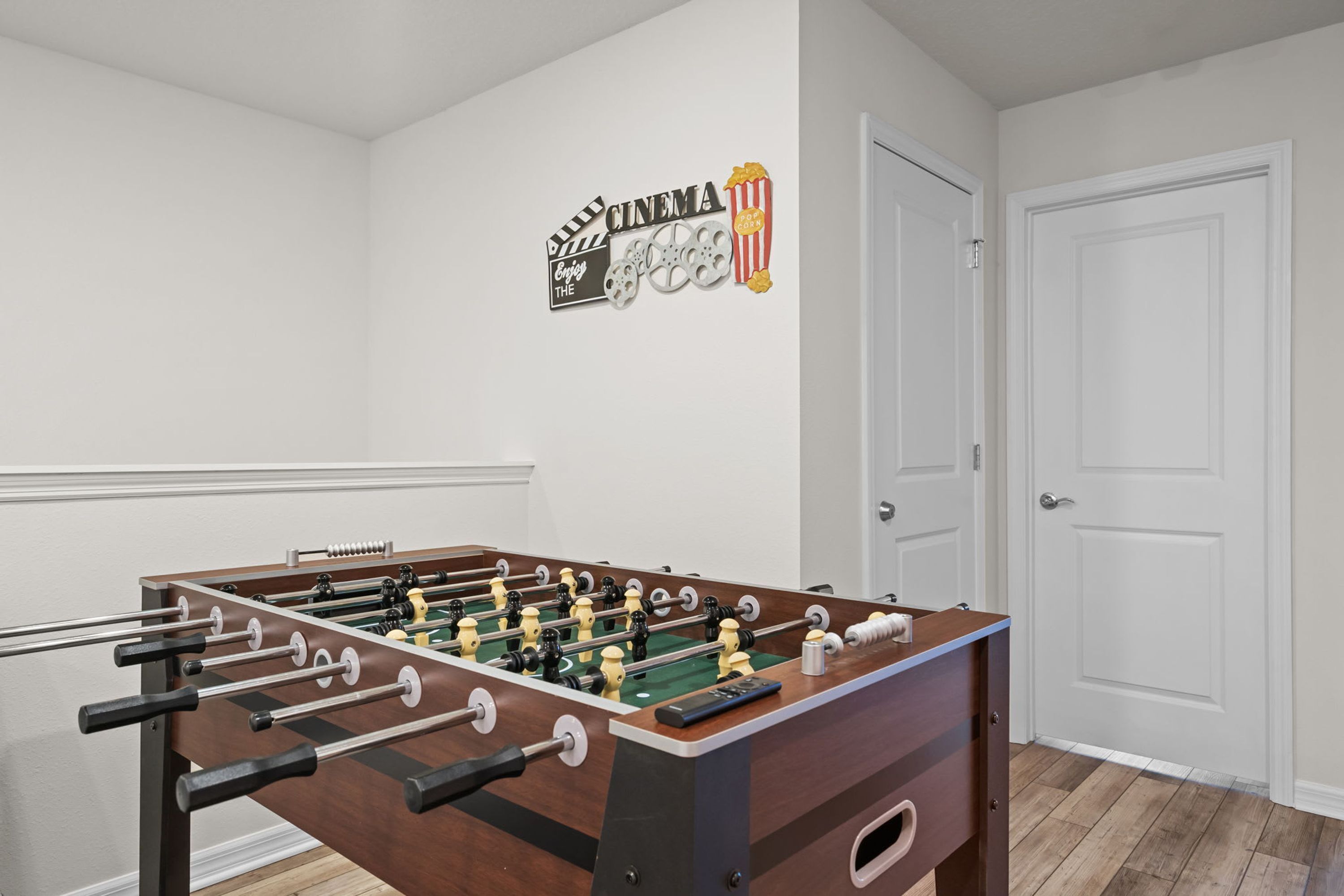 A room with a foosball table, a cinema-themed wall decoration, and a closed door.