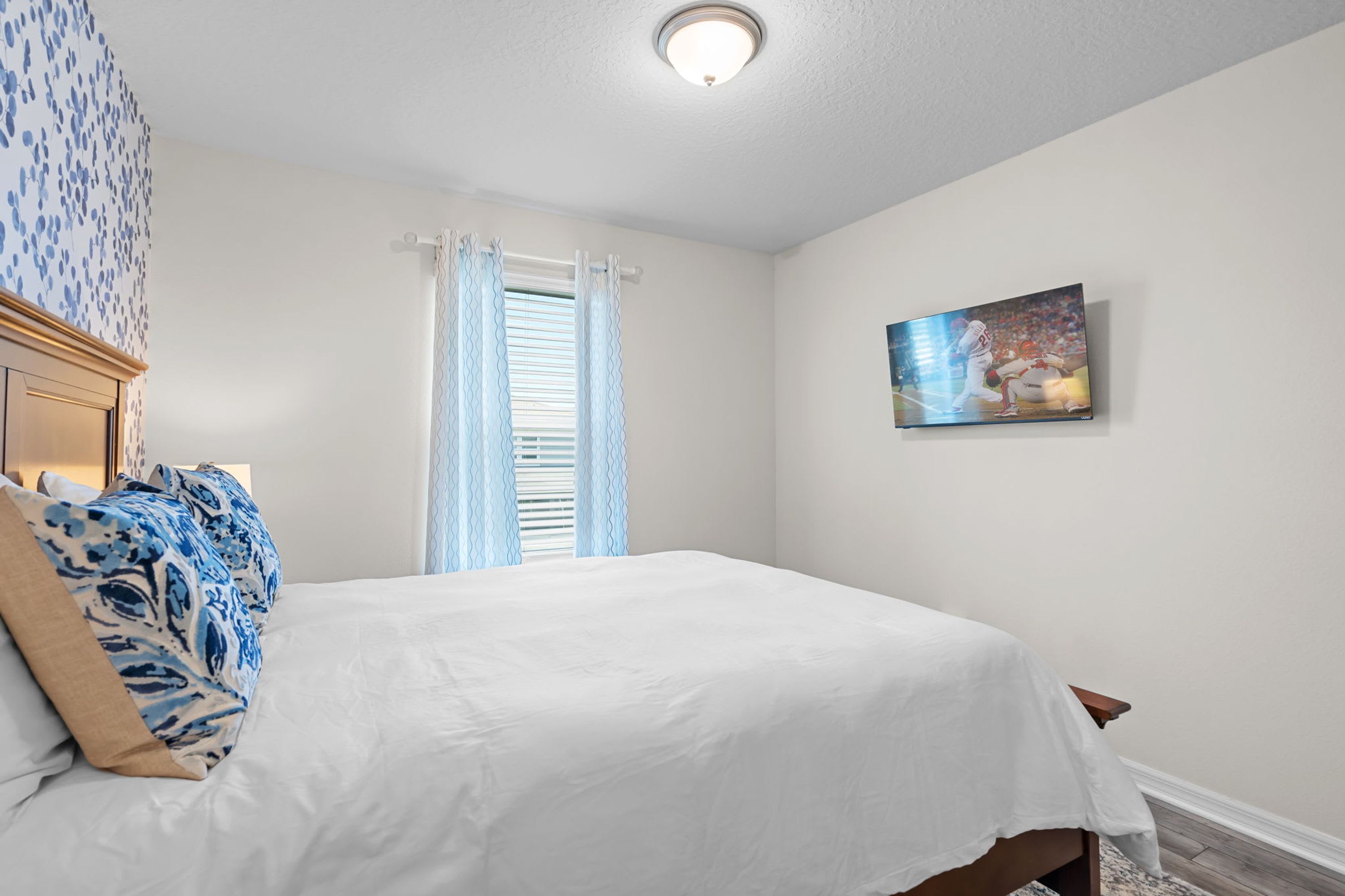 A bedroom with a bed, a headboard, a painting, and a window with curtains.