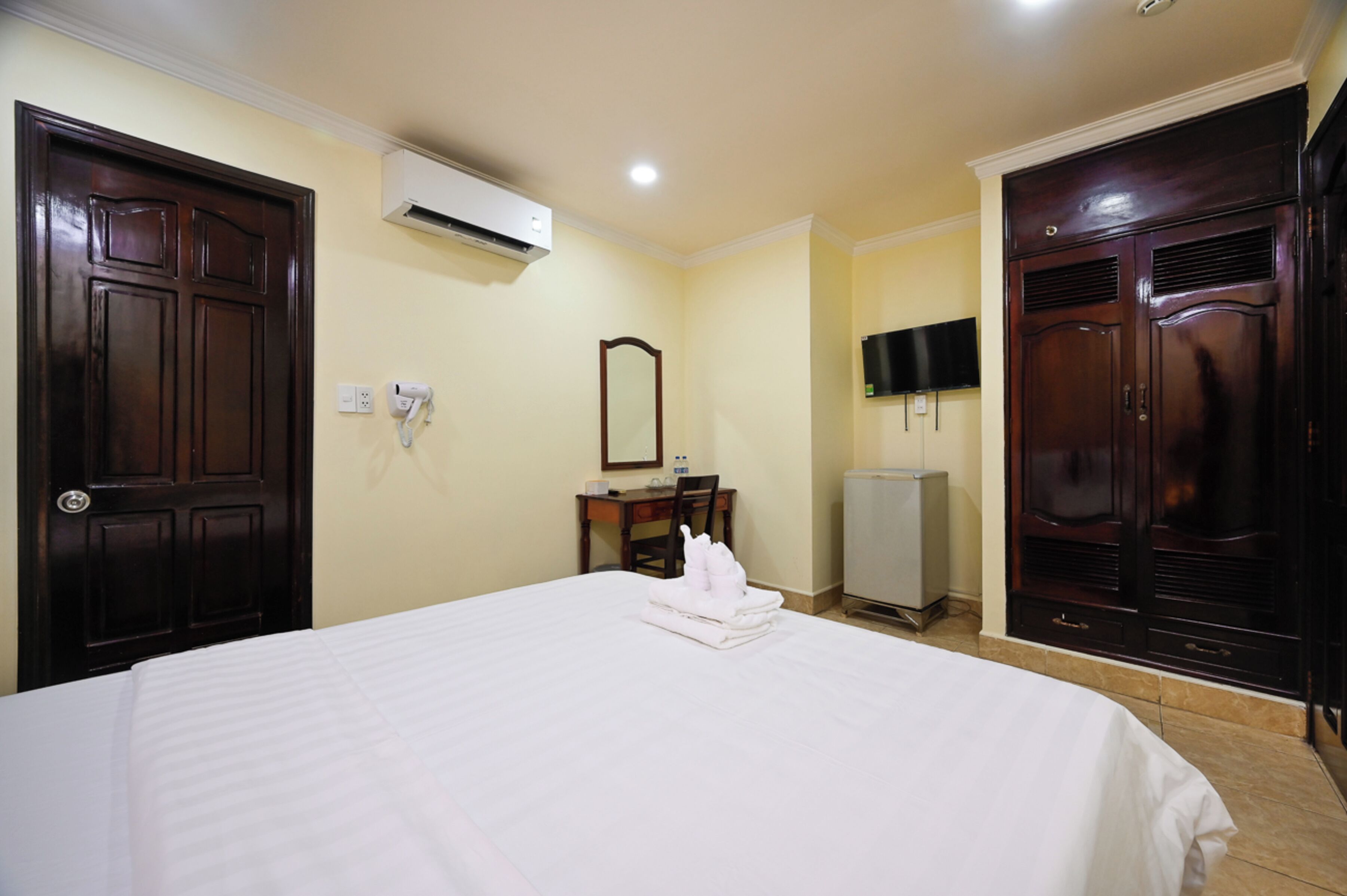 A hotel room with a large bed, a desk with a chair, a TV mounted on the wall, and a wardrobe.