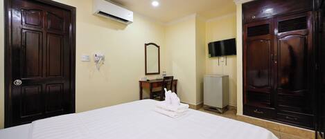A hotel room with a large bed, a desk with a chair, a TV mounted on the wall, and a wardrobe.
