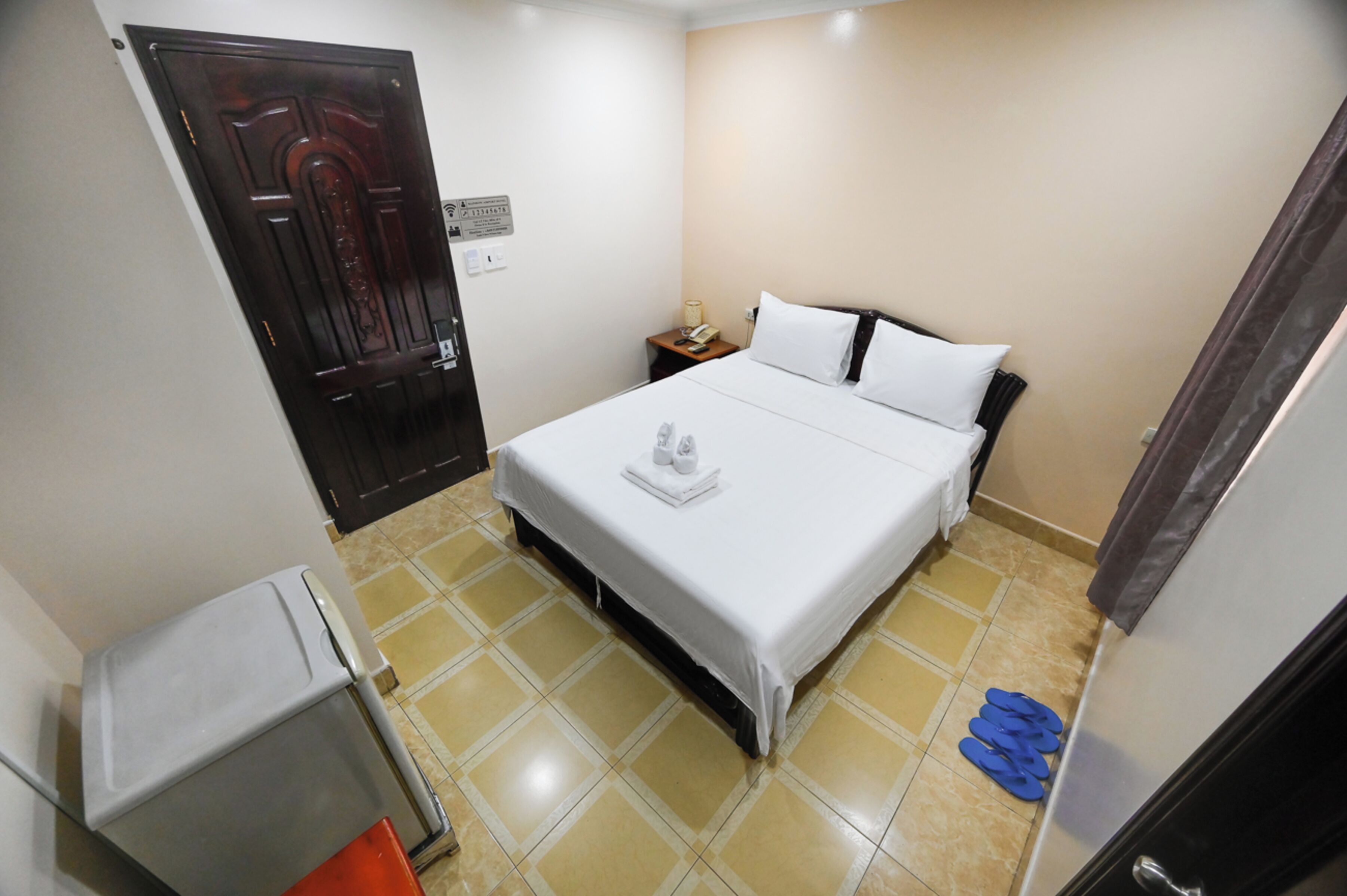 Une chambre d’hôtel avec un lit, une table de chevet, un téléphone, une porte et une petite table.