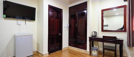 Una habitación con piso de madera, un refrigerador blanco, un escritorio de madera con una silla, un espejo grande y un armario con puerta.