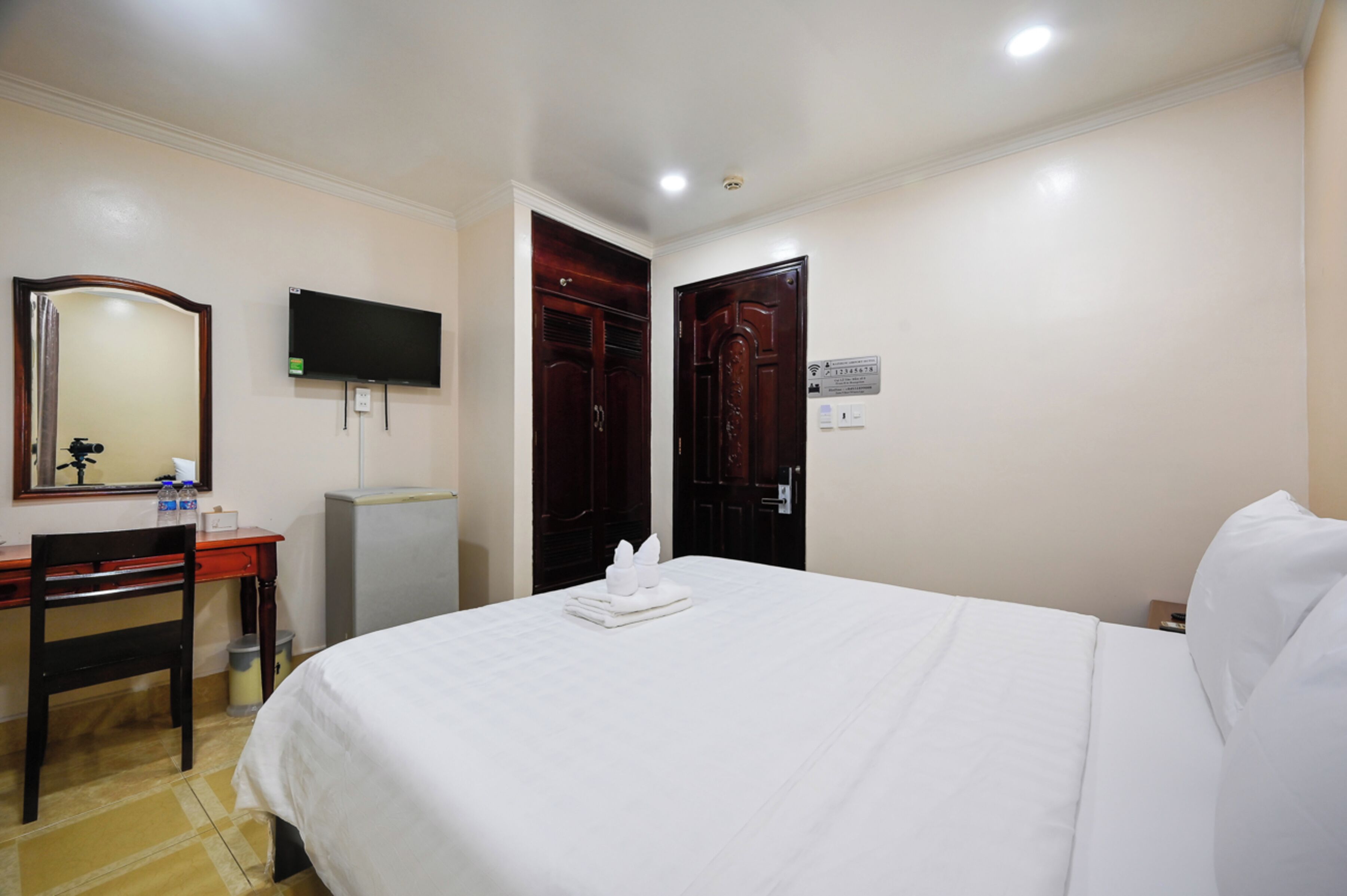 A hotel room with a bed, a desk, a chair, a television, and a wardrobe.