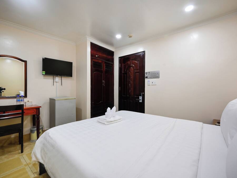 A hotel room with a bed, a desk, a chair, a television, and a wardrobe.