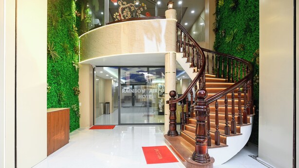 Eine moderne Hotelhalle mit einer geschwungenen Treppe, grünen Wanddekorationen und einem Empfangsschalter.