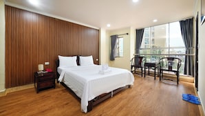 Ein Hotelzimmer mit einer Wandpaneele aus Holz, einem großen Bett mit weißer Bettwäsche, einem kleinen Tisch mit Stühlen und Blick durch ein großes Fenster.