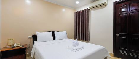 Una habitación de hotel con una cama, una mesita de noche, un equipo de aire acondicionado y una puerta de madera oscura.