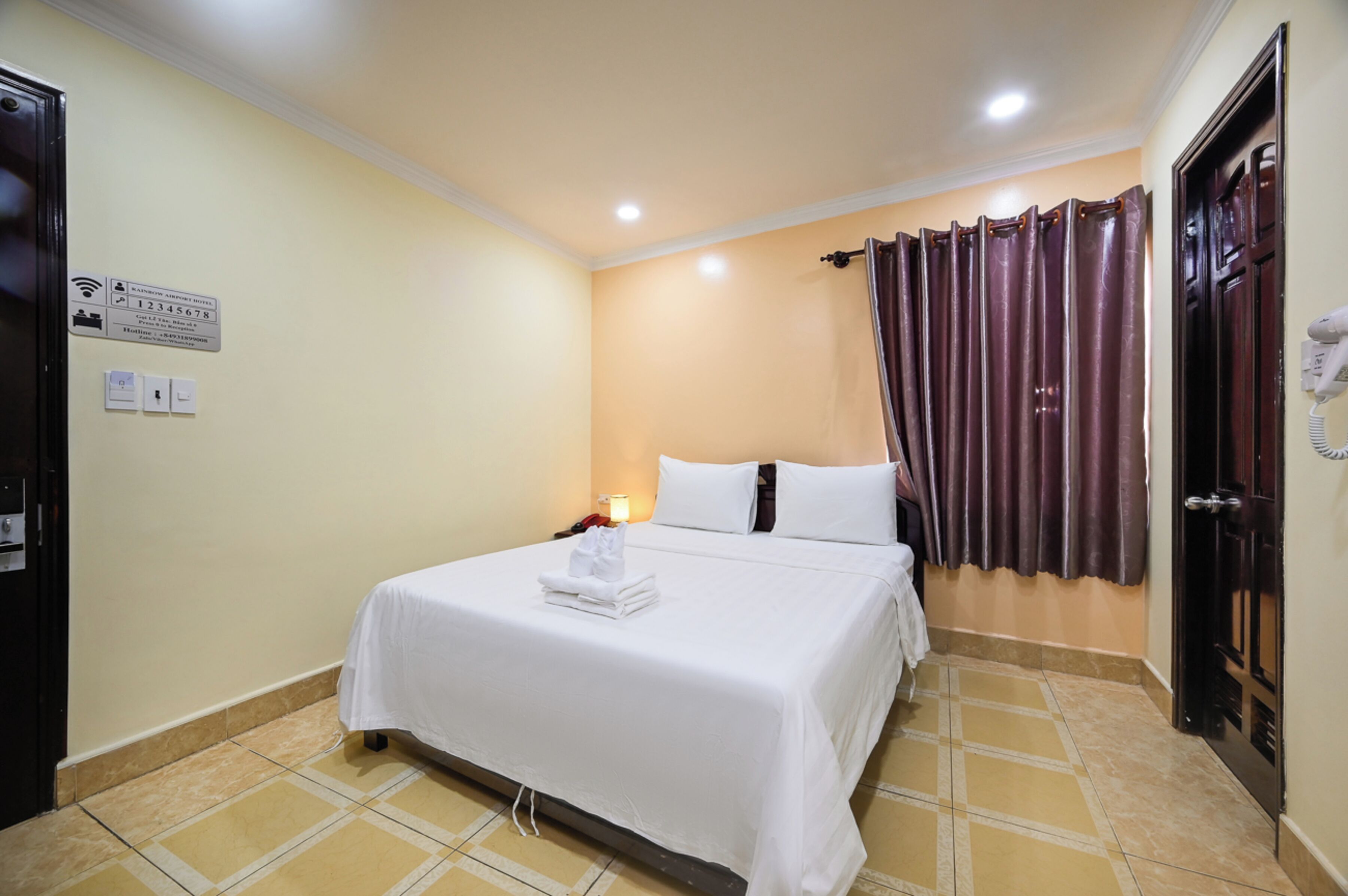 Una habitación de hotel con cama, mesita de noche, lámpara, teléfono y puerta.