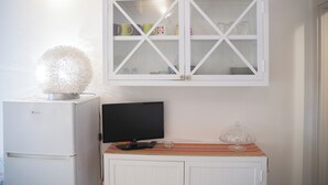 A compact kitchen with a white refrigerator, a flat-screen TV, and a cabinet with glass doors above. - The Landing, in the heart of downtown, a stone's throw from ferry and main square (Carloforte)