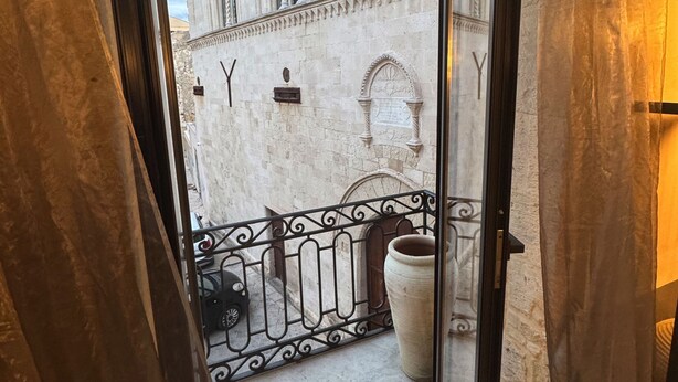 A balcony with a wrought iron railing, a large potted plant, and a view of a historic building with intricate architectural details. - Montalto Luxury House (Siracusa)