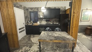 A compact kitchen with a marble countertop, a wooden-framed dining table, and a black refrigerator. - Montalto Luxury House (Siracusa)