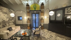 A room with a stone wall, a sofa, a coffee table, a TV, and a decorative cactus wall. - Montalto Luxury House (Siracusa)