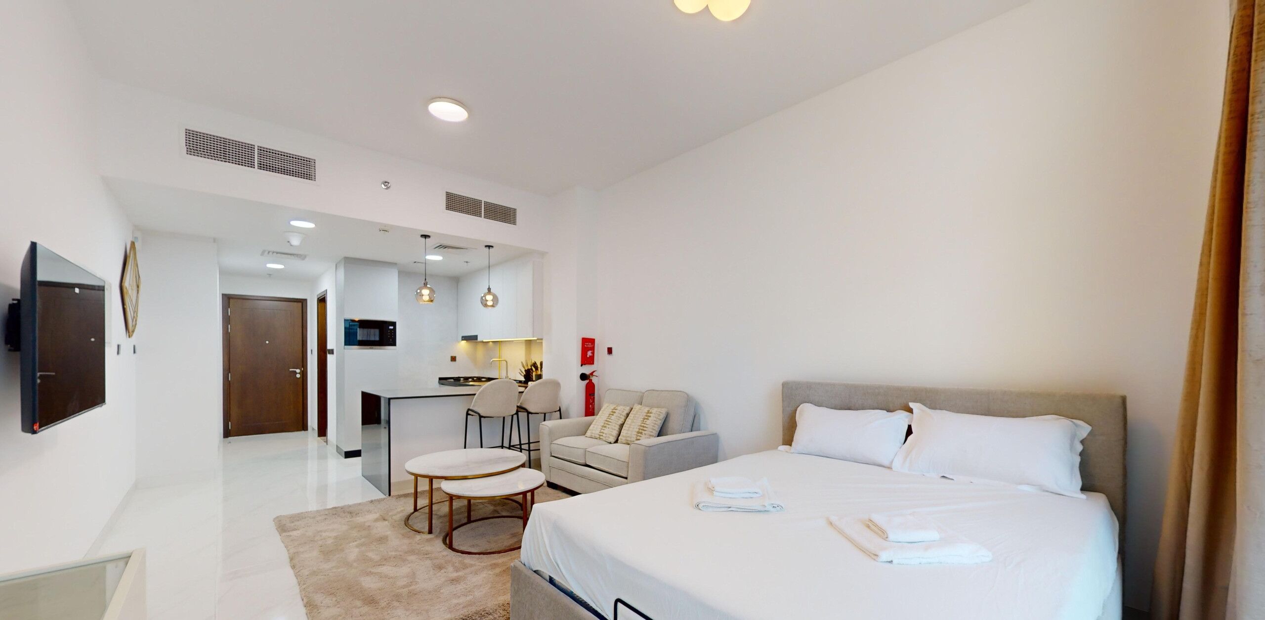 Une chambre d’hôtel moderne dotée d’un grand lit, d’un petit coin salon, d’une kitchenette et d’un téléviseur fixé au mur.